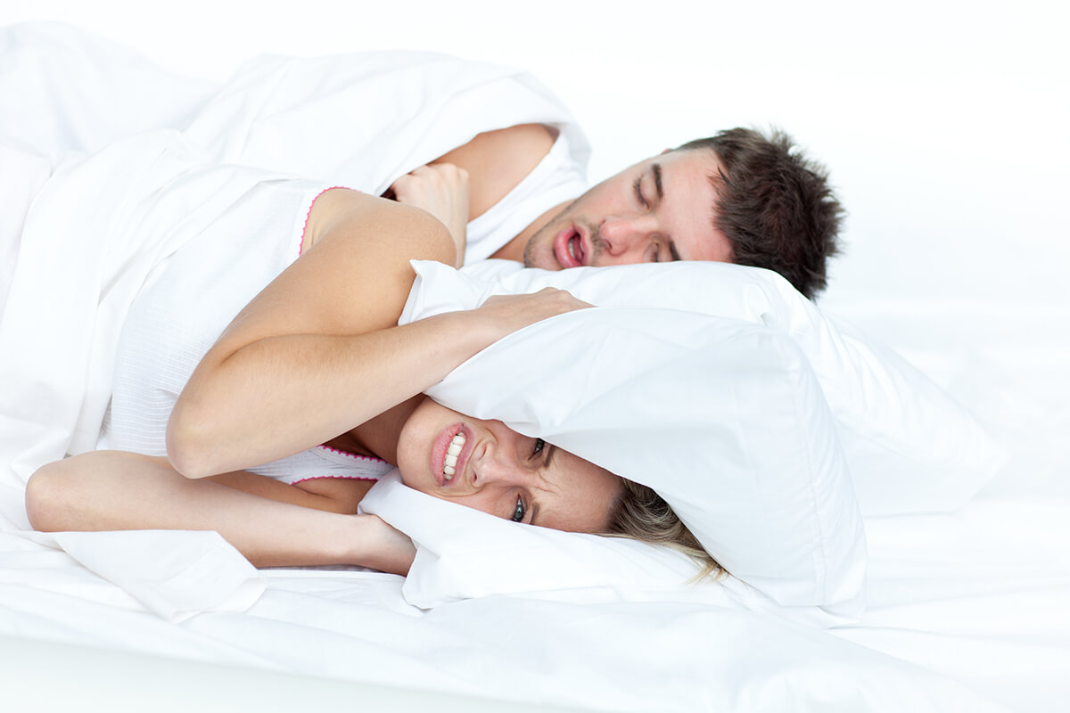 Kobieta zakrywa poduszką uszy, z powodu chrapania partnera - bezdech senny
