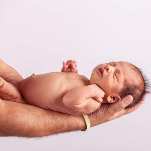 Noworodek na dłoniach mężczyzny. Poród w domu. Rozważ za i przeciw