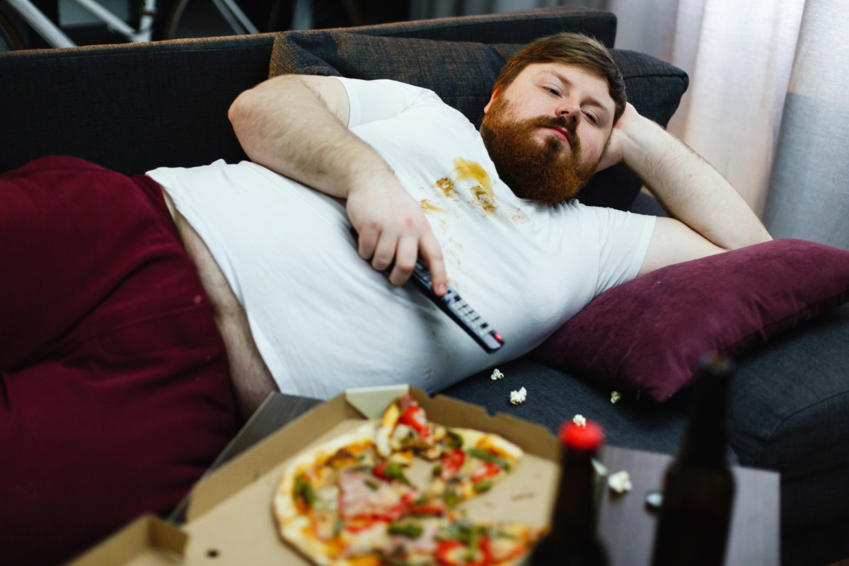 Otyły mężczyzna na łóżku przed telewizorem. Bezdech senny a otyłość - przyczyna czy skutek?