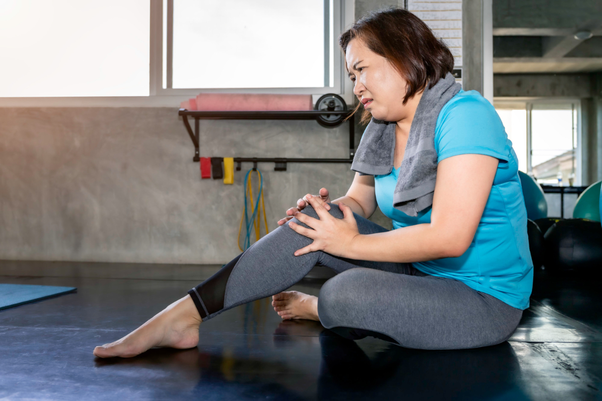 Otyła kobieta trzyma się za bolące kolano. Jak otyłość wpływa na stawy