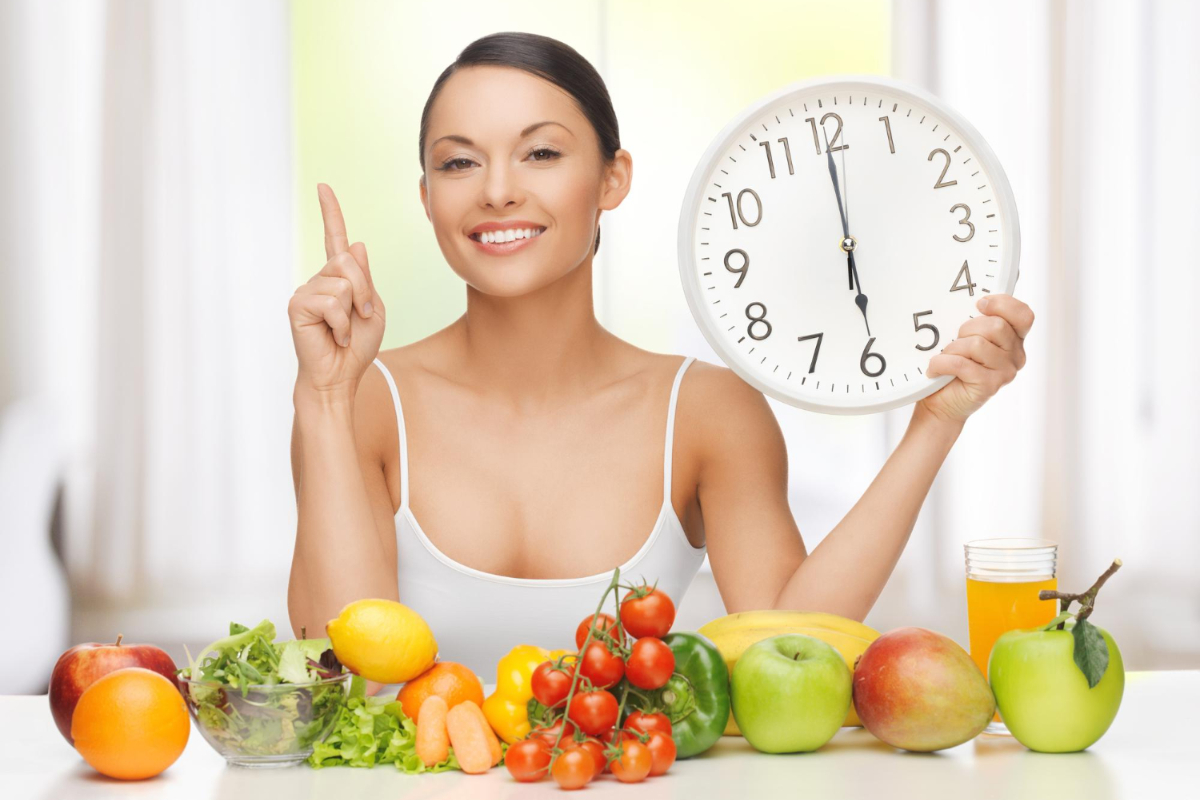 Kobieta przy stole z warzywami i owocami z zegarem w dłoni. Post przerywany