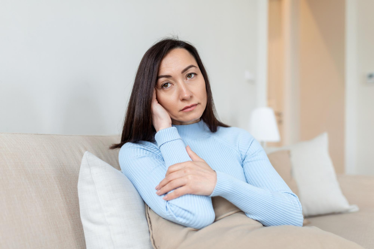Smutna kobieta na łóżku. Przedwczesna niewydolność jajników — czym może być spowodowana