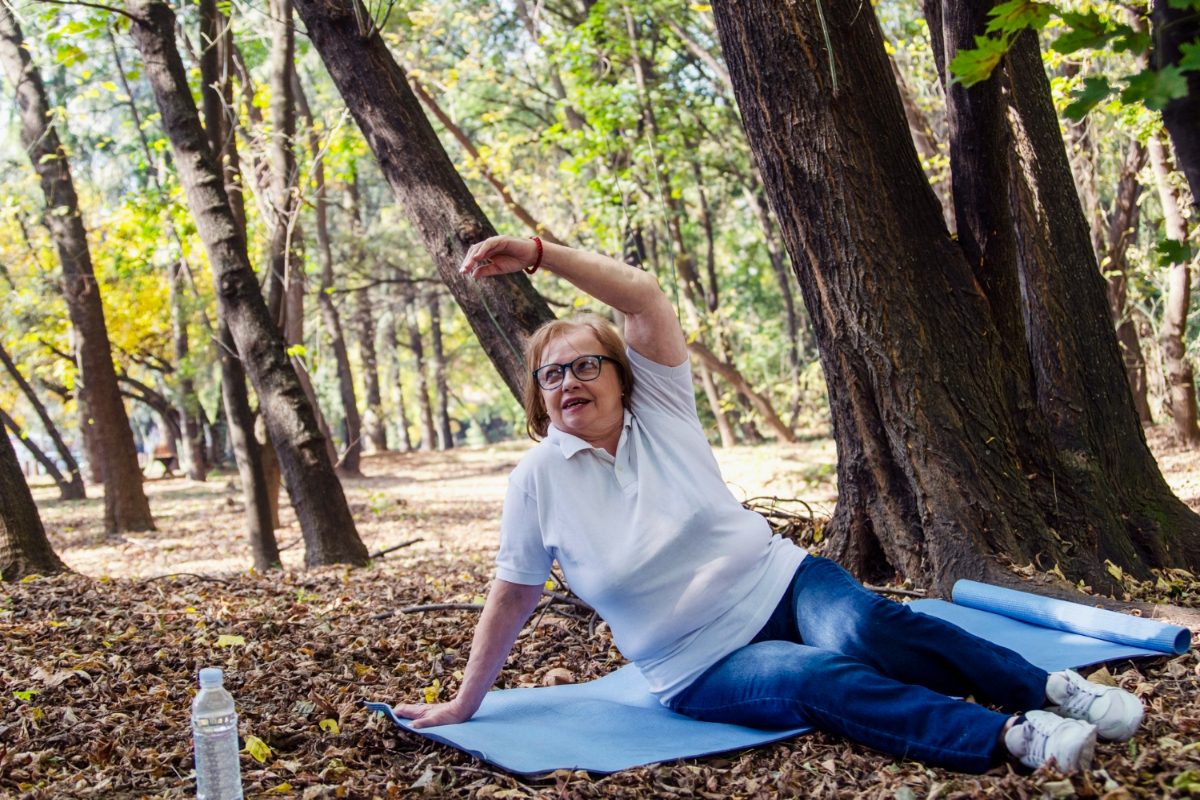 Starsza kobieta ćwiczy na macie w lesie