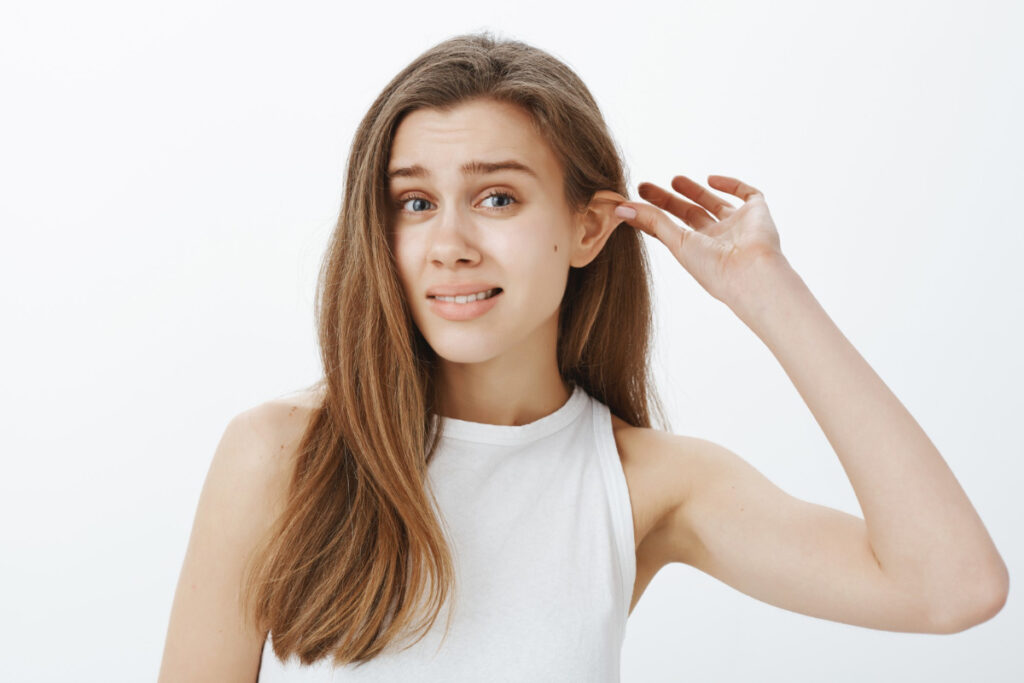 Kobieta trzyma się za odstające ucho. Korekcja uszu — dlaczego warto z niej skorzystać