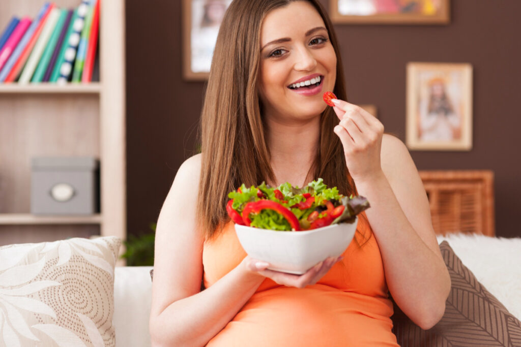 Uśmiechnięta kobieta w ciąży je sałatkę warzywną. Dieta młodej matki
