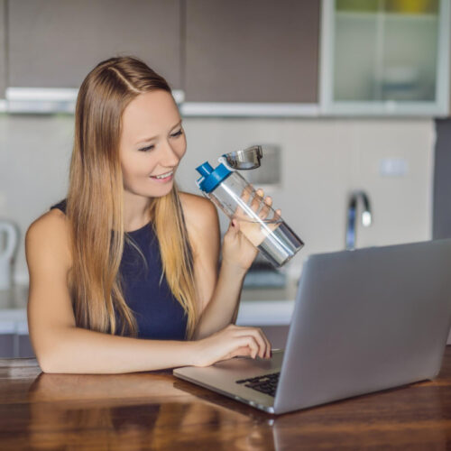 Kobieta pije wodę pracując przy laptopie - picie wody codziennie