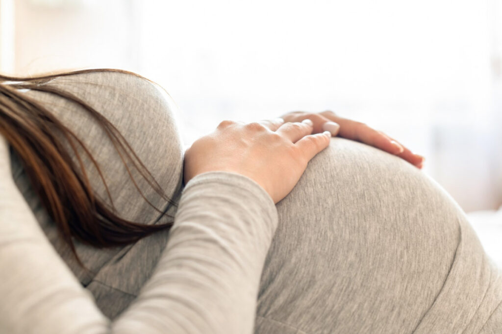 Kobieta w ciąży z dłońmi na brzuchu - Późne macierzyństwo — jakie ryzyko ze sobą niesie