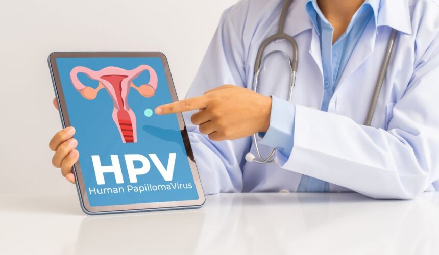 Lekarka wskazuje na grafikę z macicą kobiety i napisem HPV - Wirus HPV - objawy, leczenie, zapobieganie