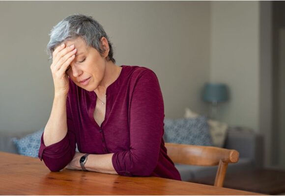 Kobieta z bolącą głową siedzi przy stole. Zmiany u kobiet po 40. roku życia