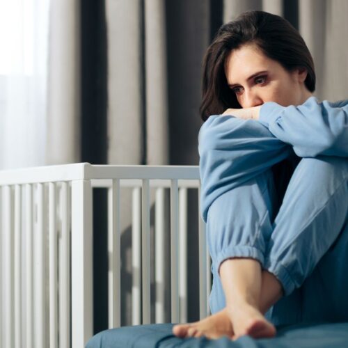 Smutna kobieta na łóżku obok pustego łóżeczka - Poronienia nawracające – przyczyny, diagnostyka i wsparcie