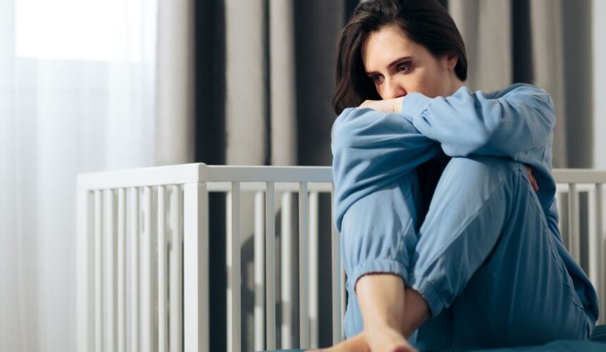 Smutna kobieta na łóżku obok pustego łóżeczka - Poronienia nawracające – przyczyny, diagnostyka i wsparcie