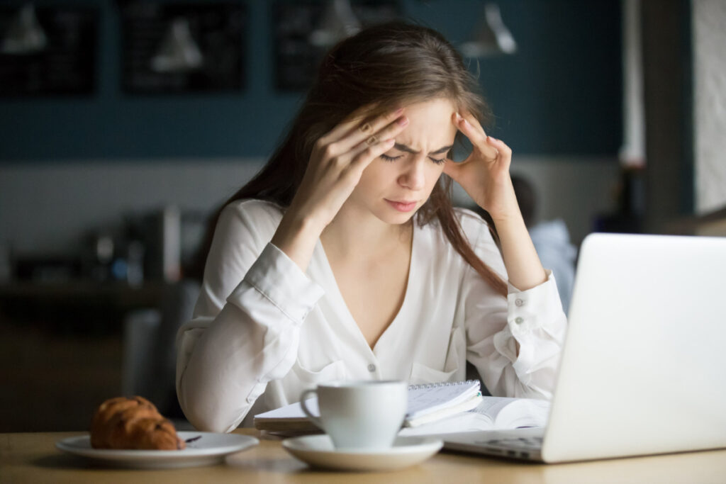 Kobieta przy laptopie z dłońmi przy skroniach - migrena - przyczyny