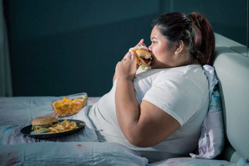 Otyła kobieta w łóżku je niezdrowe potrawy typu fast food
