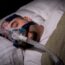 Mężczyzna śpi w masce CPAP. Obturacyjny bezdech senny — kto jest na niego narażony